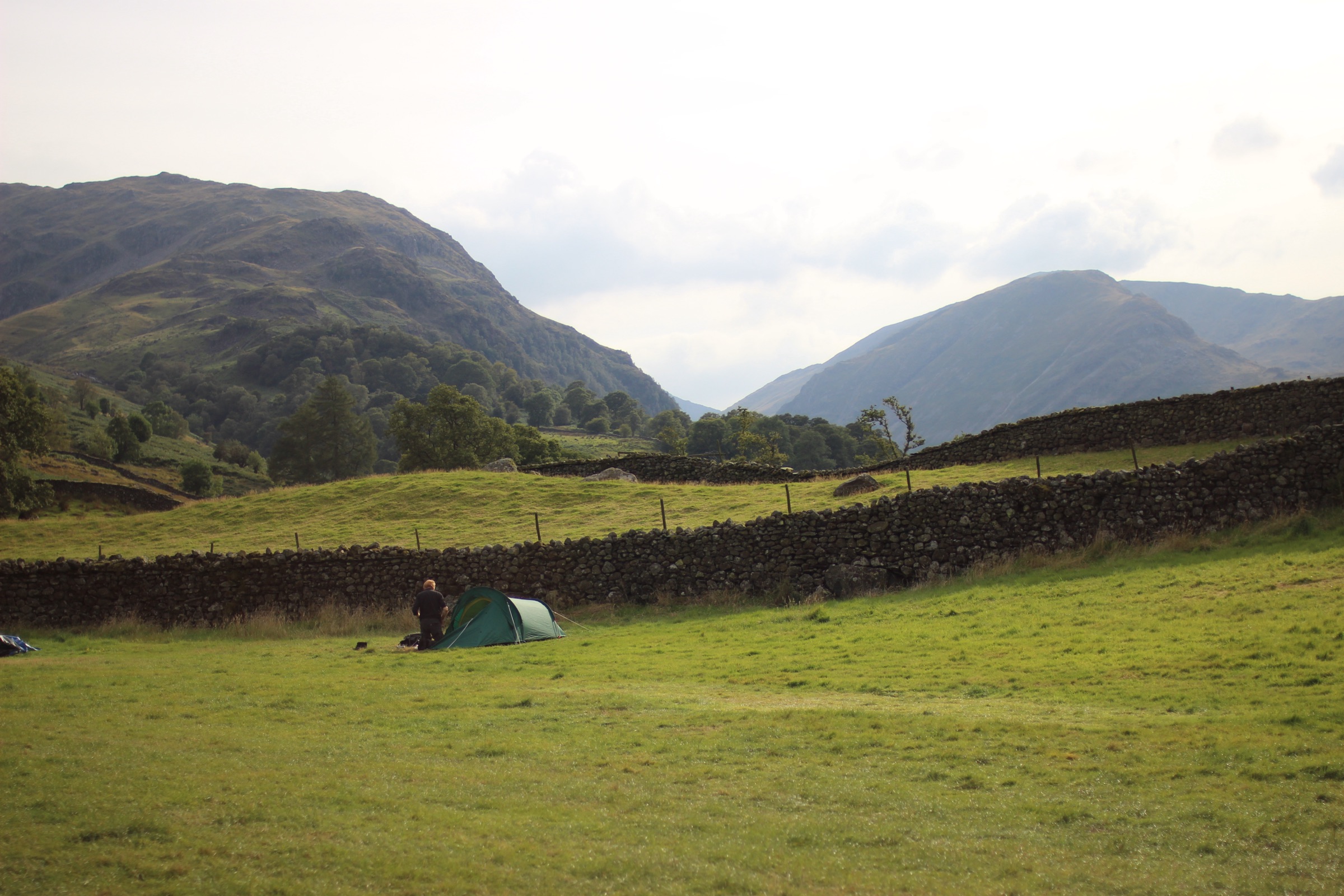 A green tent pitched by a drystone wall in a Lake District valley, fells rising behind